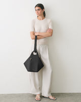Person leans against wall holding a geometric handbag and wearing a casual outfit.