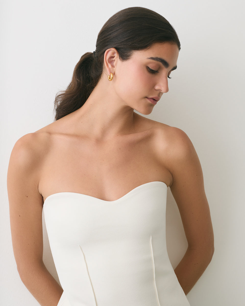 Woman wearing strapless top with gold hoop earrings facing down.