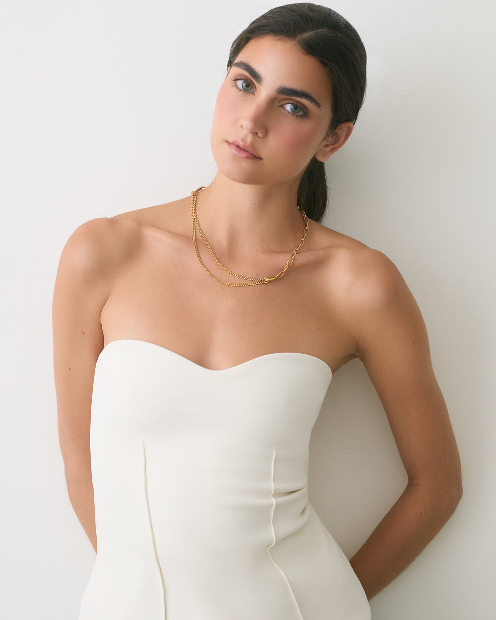 Person wearing a strapless top and necklace, leaning against a wall.