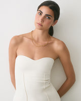 Person wearing a strapless top and necklace, leaning against a wall.