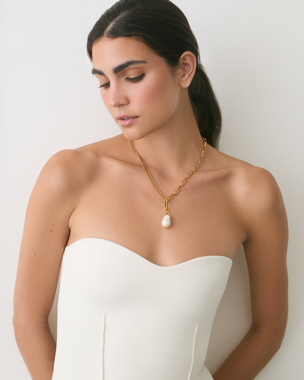 Person wearing a strapless top and a necklace with a pendant.