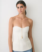 Person wearing a strapless top with long necklace standing against a wall.