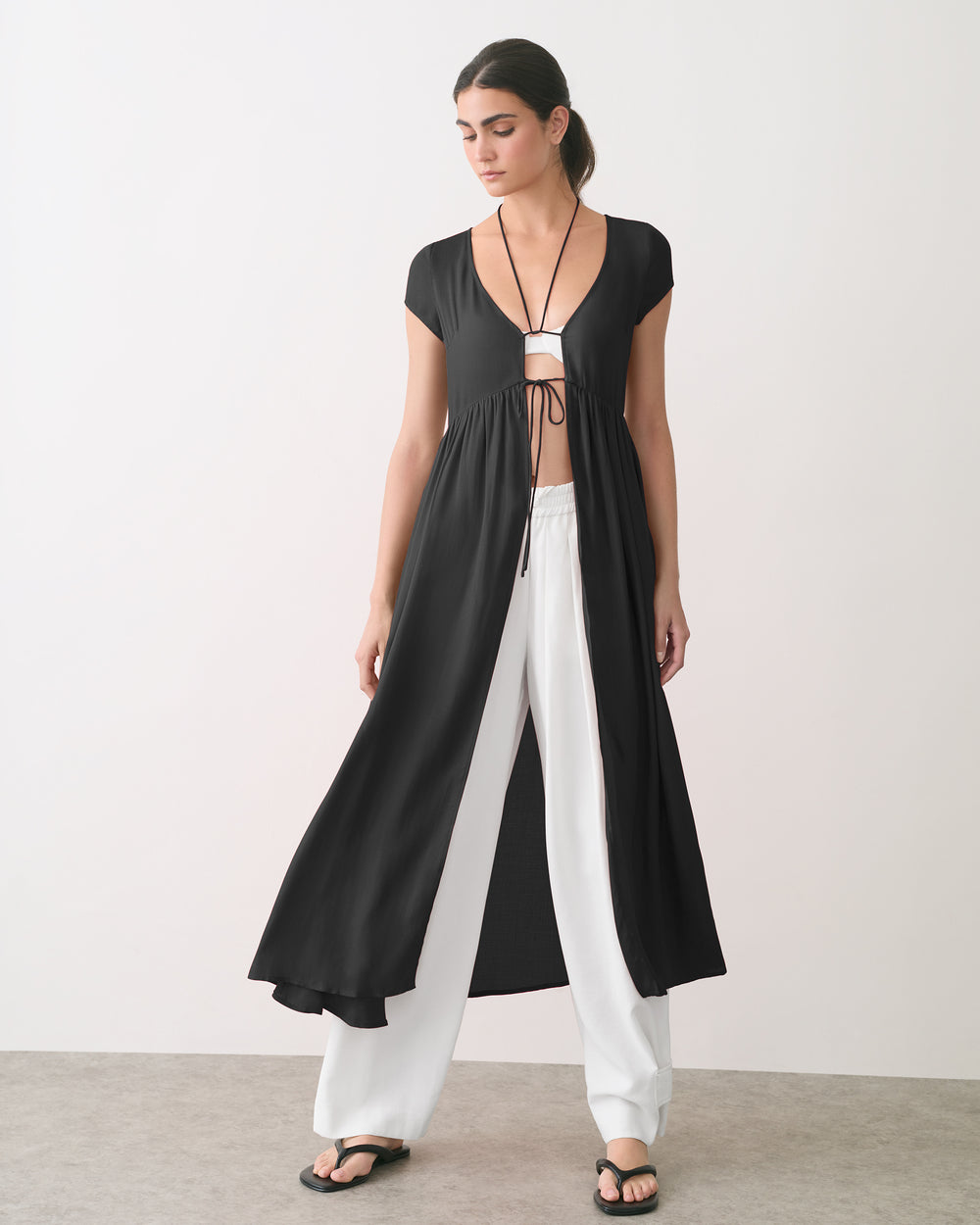 Person wearing a long open cardigan over a top and wide-leg pants, with sandals.