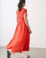 Woman in a flowing dress over pants, walking away in a minimalistic space.