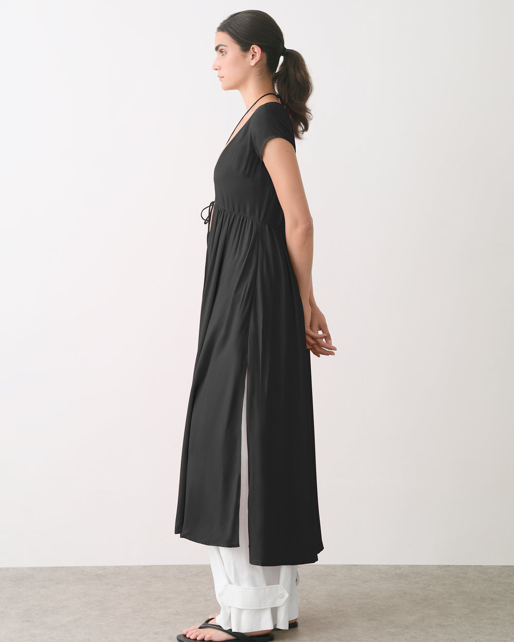 Person in long dress over wide pants, standing sideways in an indoor setting.