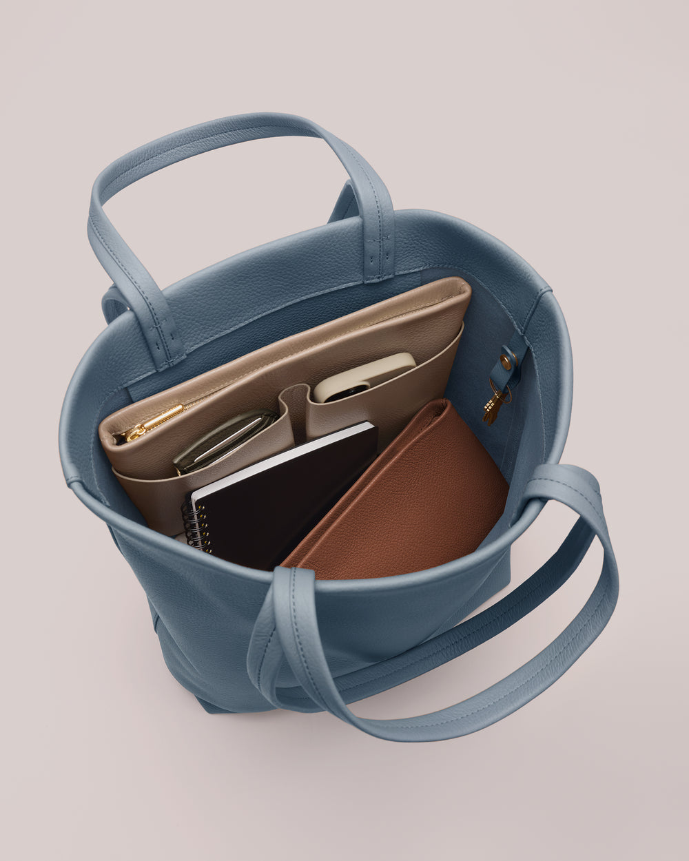 Open handbag with organized items inside, including notebooks and phone.