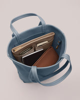 Open handbag with organized items inside, including notebooks and phone.