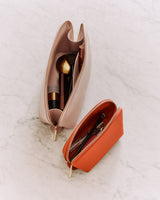 Two open cosmetic bags with makeup items inside on a surface.