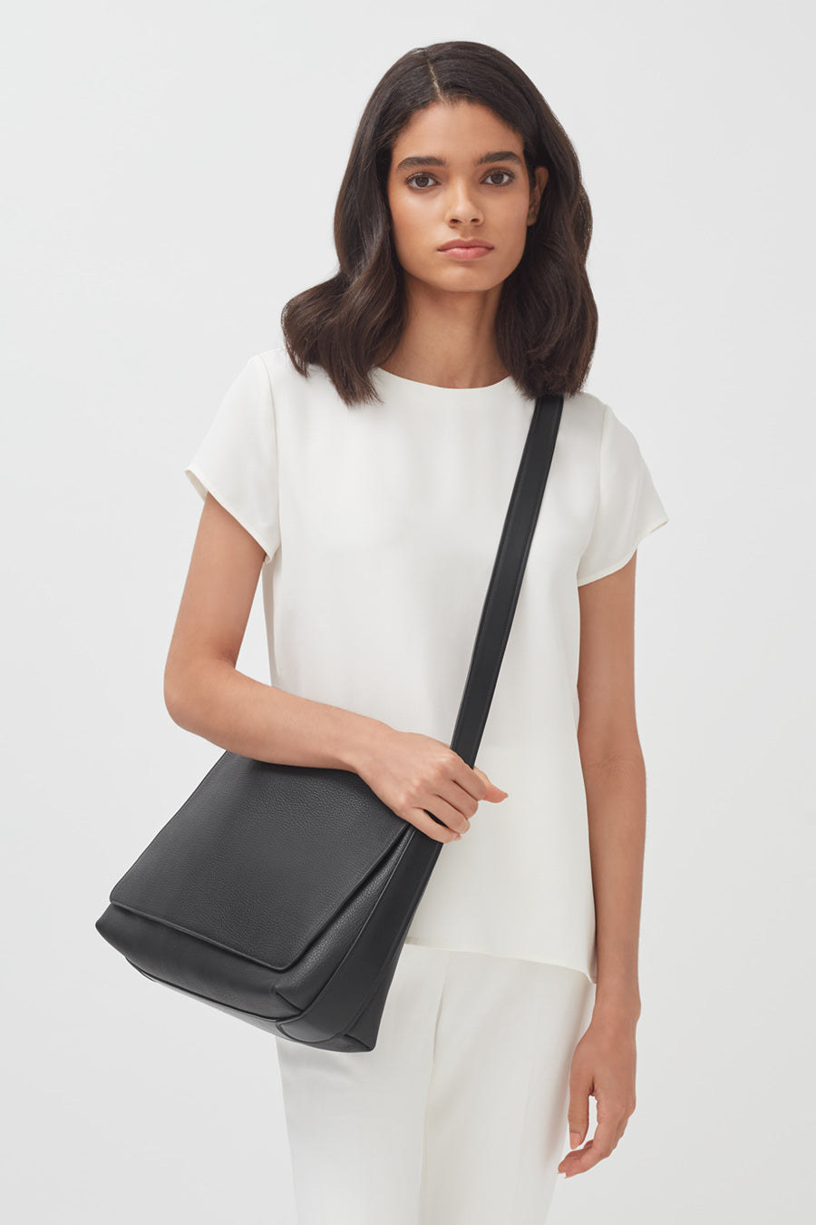 Woman standing with a shoulder bag, looking at the camera.