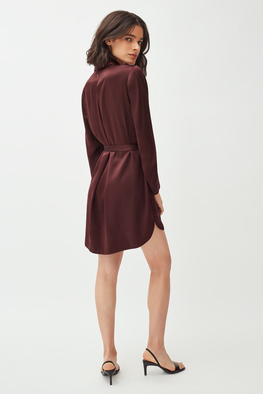 Woman standing, looking over shoulder, wearing a dress and heels.