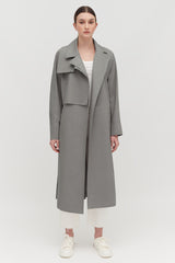 Person wearing a long coat over a top and pants, standing against a plain background.