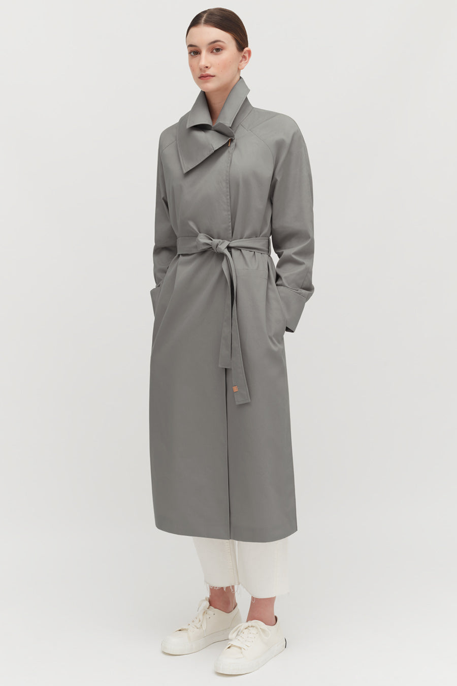 Person wearing a long belted coat, white pants, and sneakers.