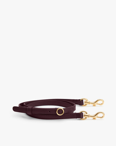 Adjustable shoulder strap with gold clasps placed on a plain background.