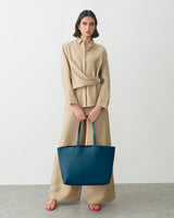 Person holding a large tote bag standing against plain background.