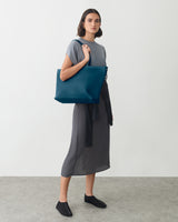 Person holding tote bag, wearing dress and shoes, standing on indoor floor.