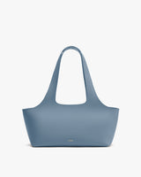 Handbag with long shoulder straps placed on a plain background.
