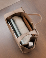 Open tote bag containing a sweater, books, and a thermos on a wooden floor.