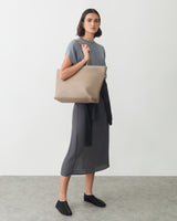 Person holds large tote bag, wearing a casual outfit with a garment draped over shoulder.