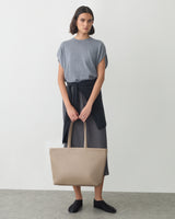 Person holding a tote bag with a long-sleeve shirt tied around waist