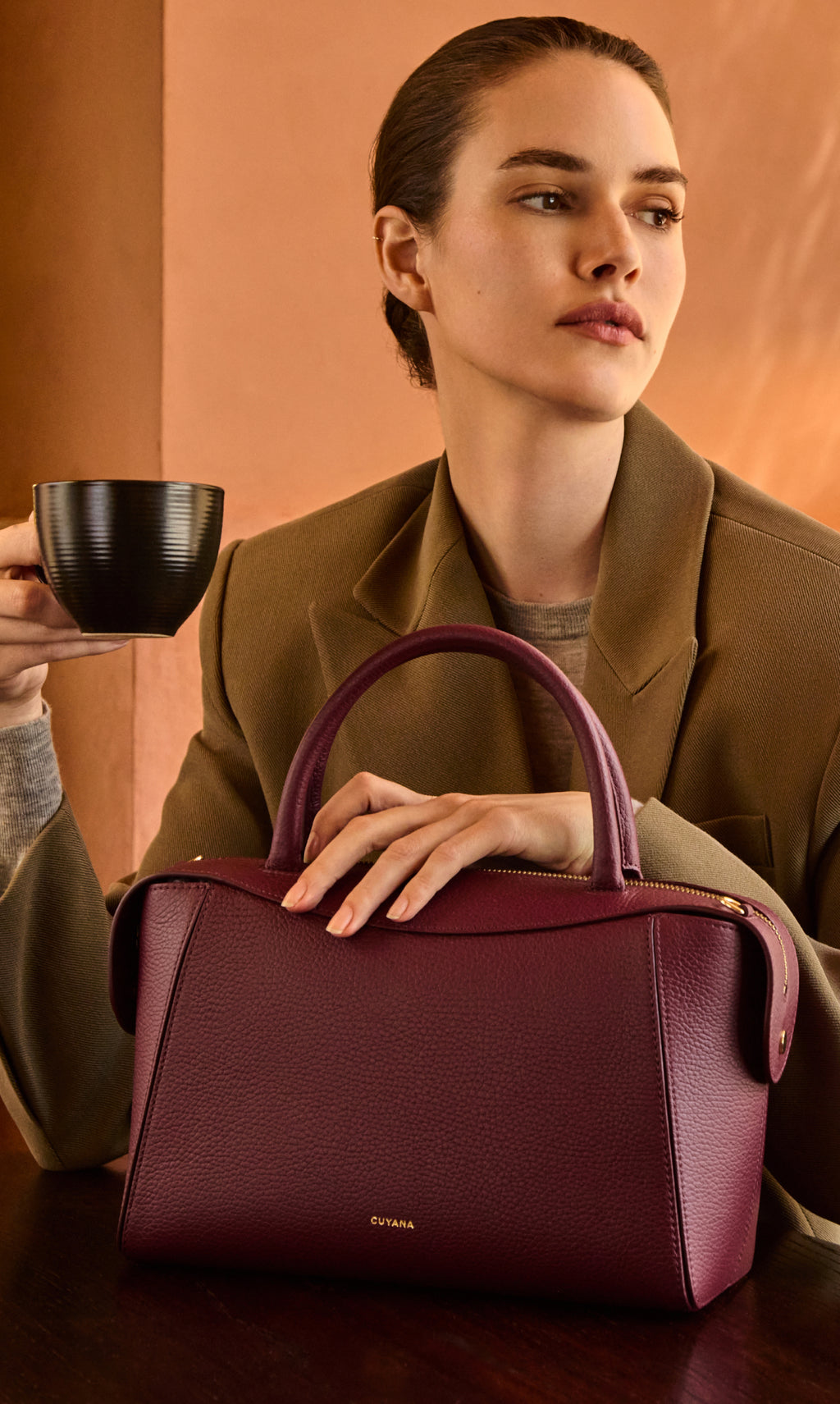Person holding a cup seated at a table with a handbag