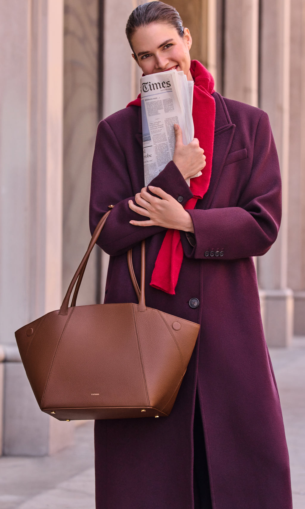 Person holding newspaper and handbag, standing outside.