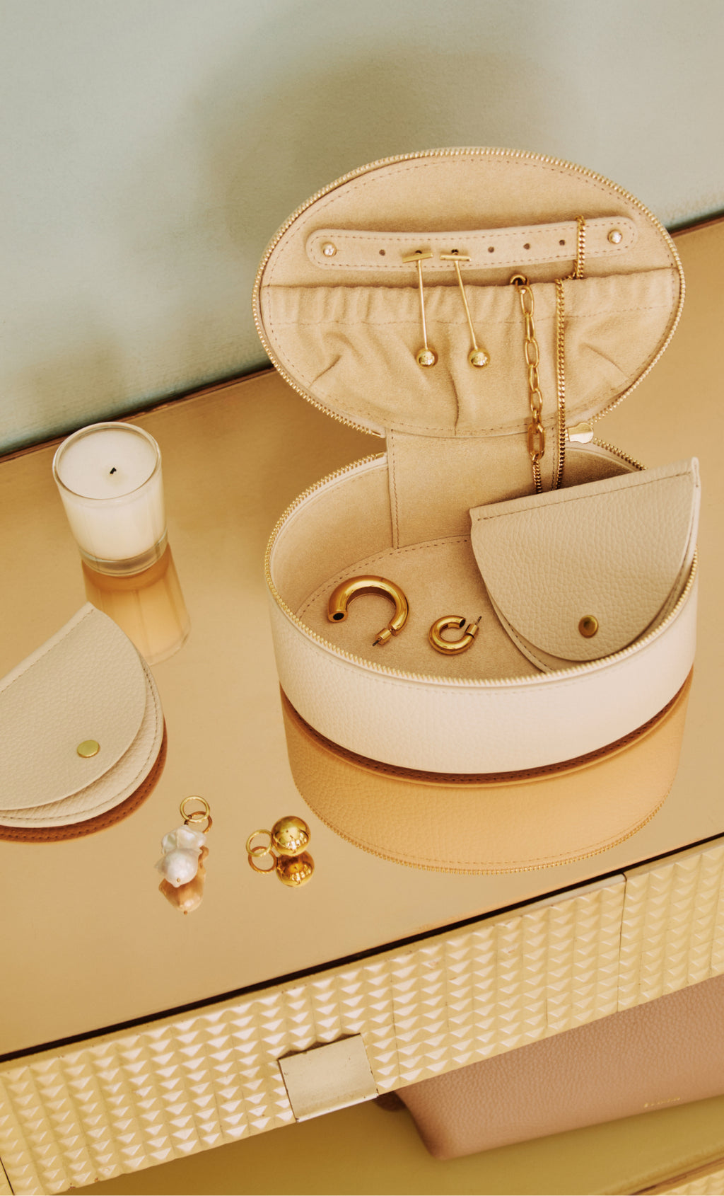 Jewelry box with earrings, necklace, candle, small pouch, and rings on a reflective surface.