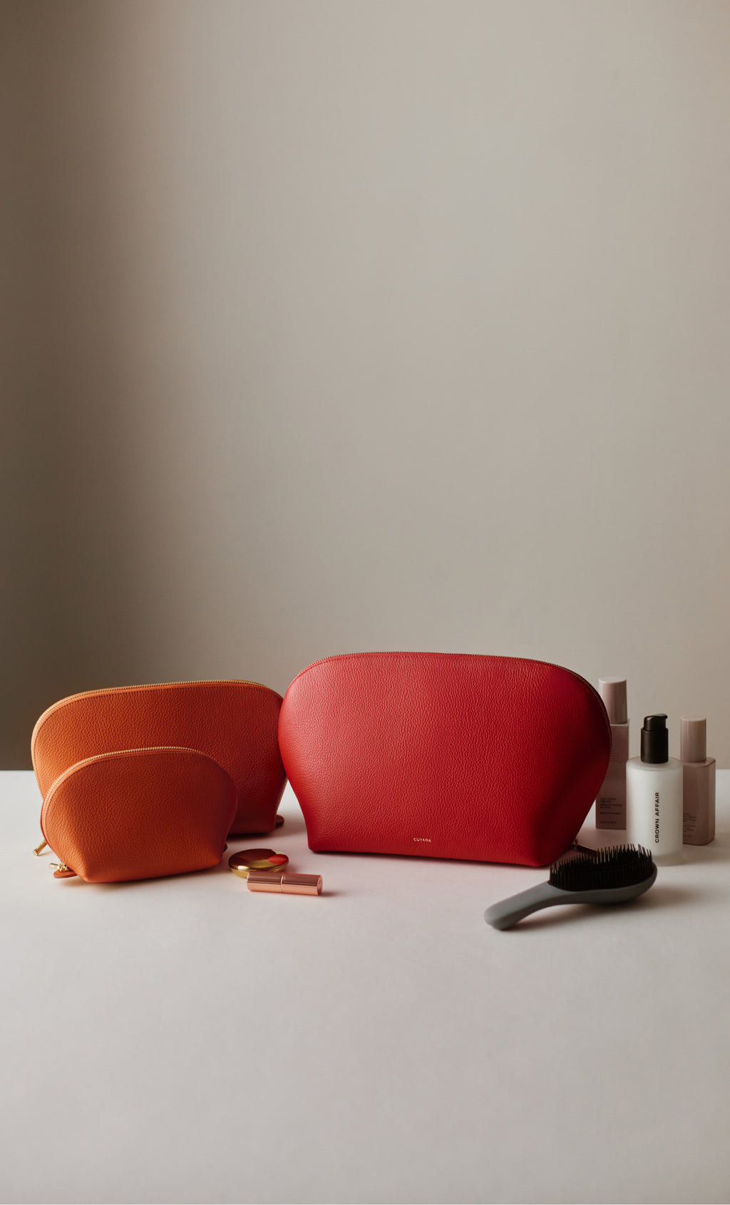 Three cosmetic bags with lotions and a brush in the background.