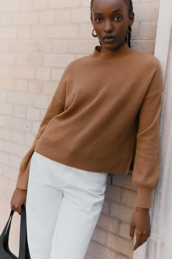 Woman standing against a brick wall holding a bag