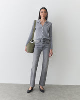 Person wearing shirt and jeans, holding a shoulder bag and standing indoors.