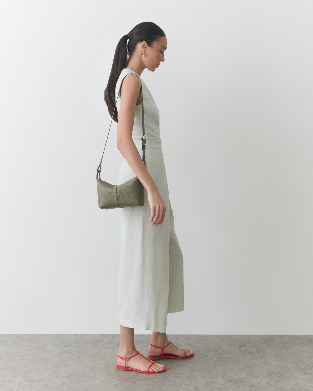 Person in long dress with shoulder bag and sandals stands sideways.
