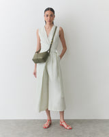 Person in sleeveless outfit with a crossbody bag and sandals.