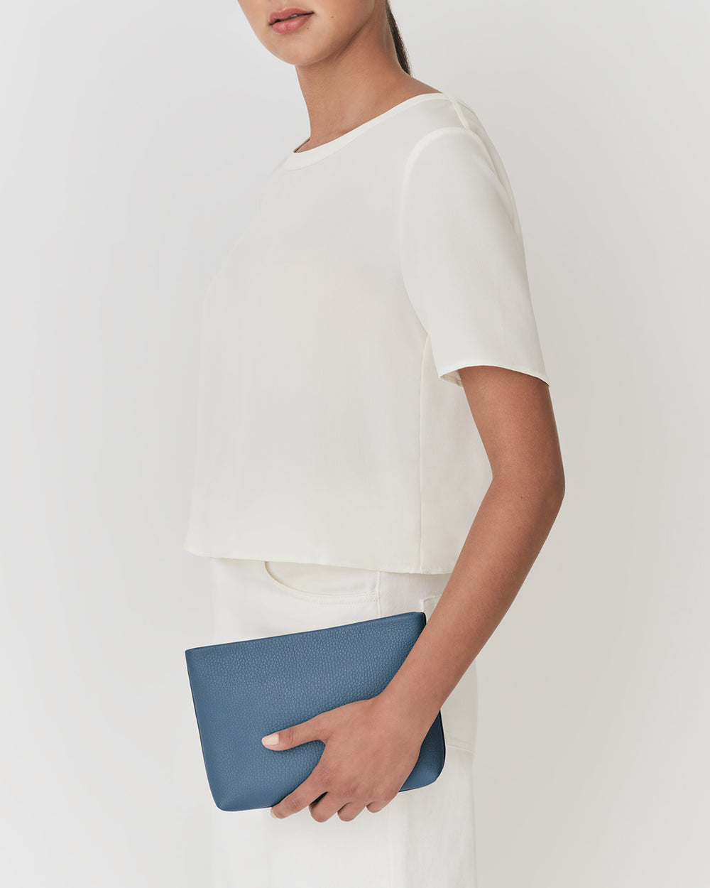 Person holding a clutch bag, wearing a short-sleeve top.