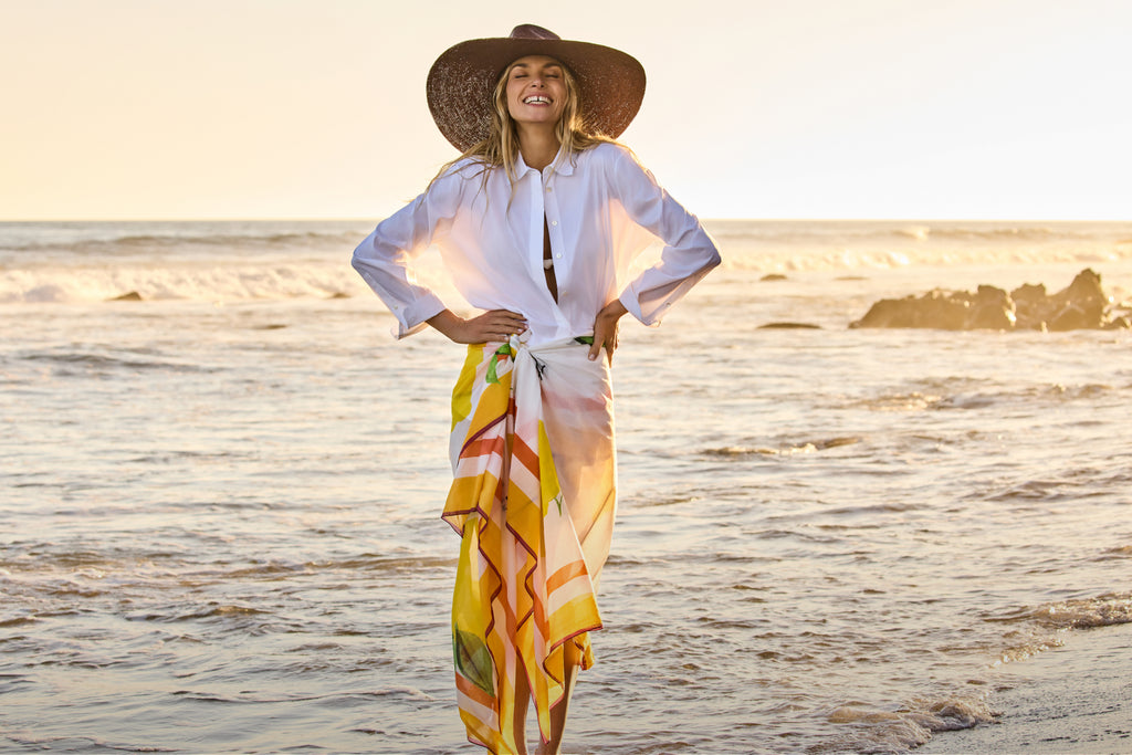 Person on beach wearing large hat and wrap skirt with arms on hips.
