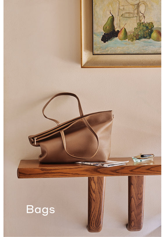 Handbag on a wooden shelf below a fruit painting.