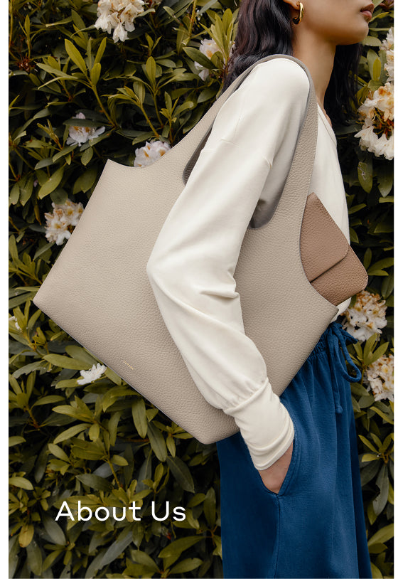 Person holding a large tote bag over shoulder near leafy bushes.