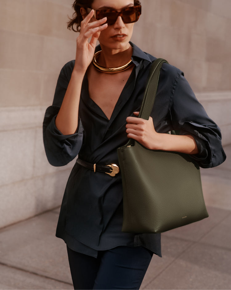 Person wearing sunglasses and accessorized outfit, holding shoulder bag.