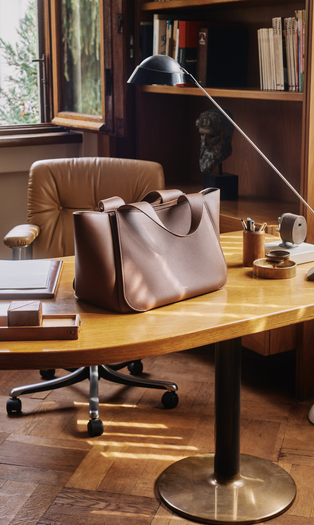 Large bag on a wooden desk with books and office supplies nearby.