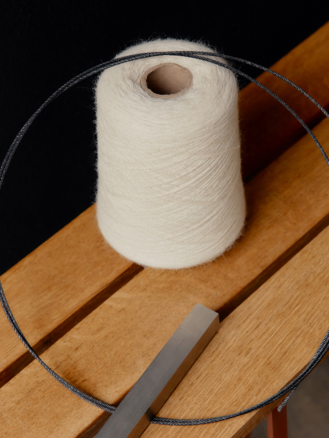 A spool of thread on a wooden surface with a metal bar nearby.