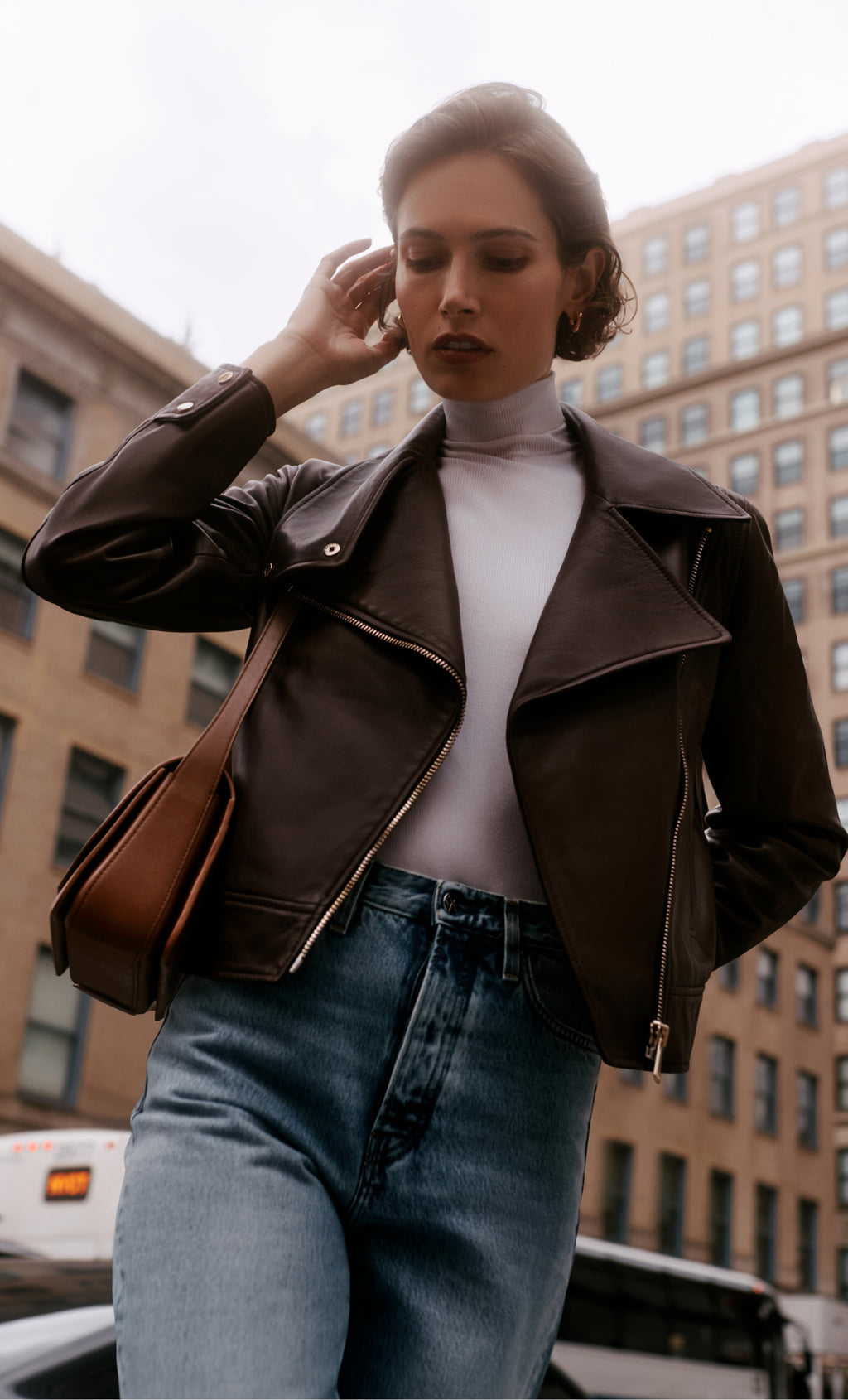 Person wearing a jacket and jeans, carrying a shoulder bag in a city setting.