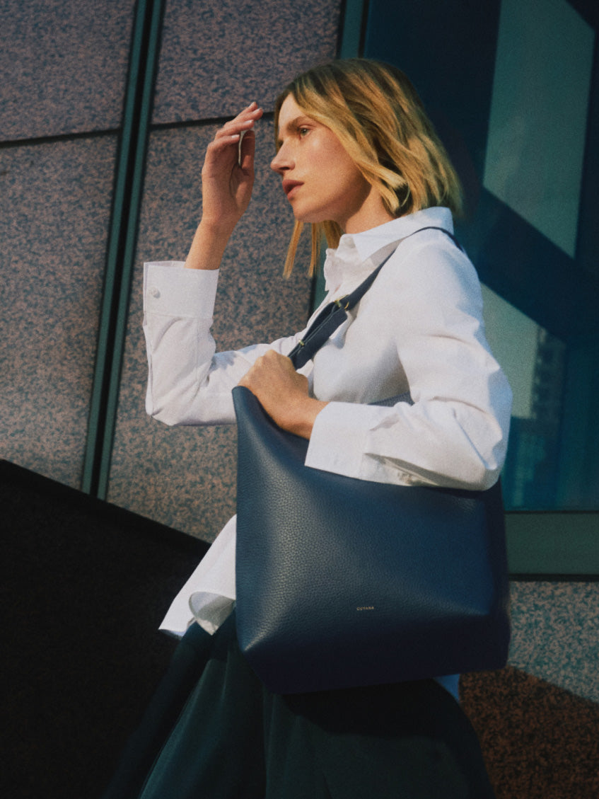 Person holding shoulder bag outside modern building.