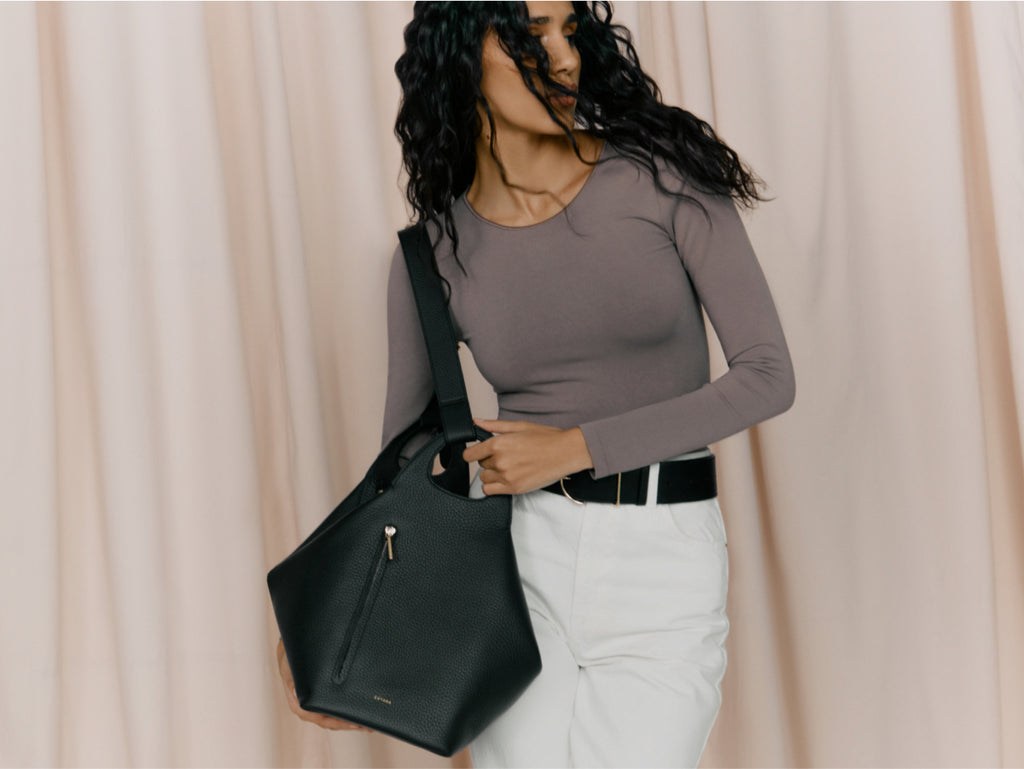 Woman holding a handbag, standing against a draped background.