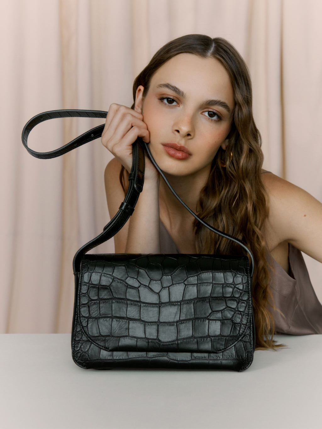 Woman posing with a handbag, resting her chin on the strap.