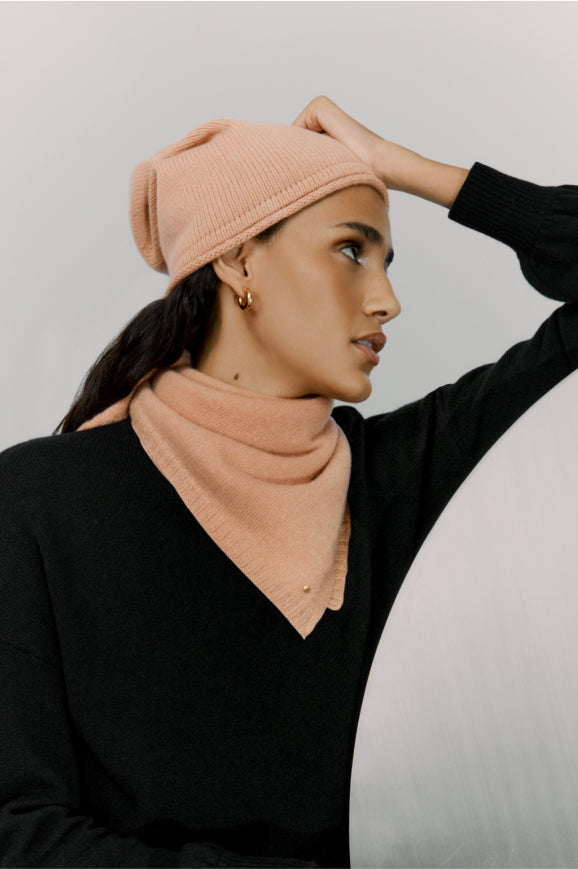 Woman wearing a beanie and turtleneck, looking away and touching her hat.