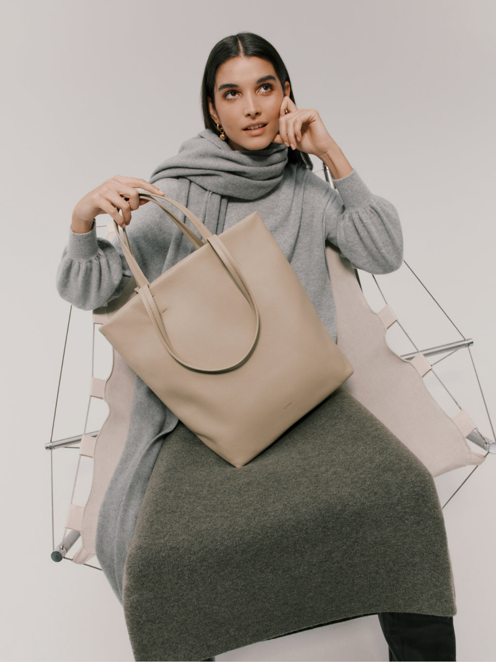 Woman sitting, holding a large bag, looking thoughtful.