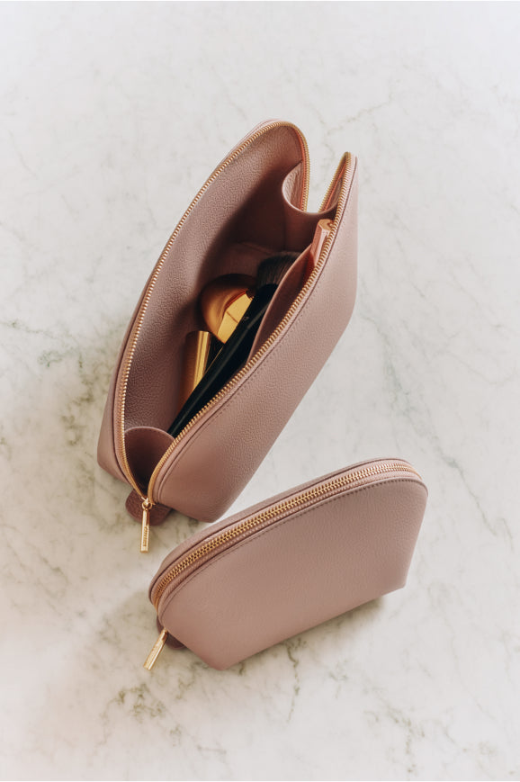 Two makeup bags with one open showing contents on a marble surface.