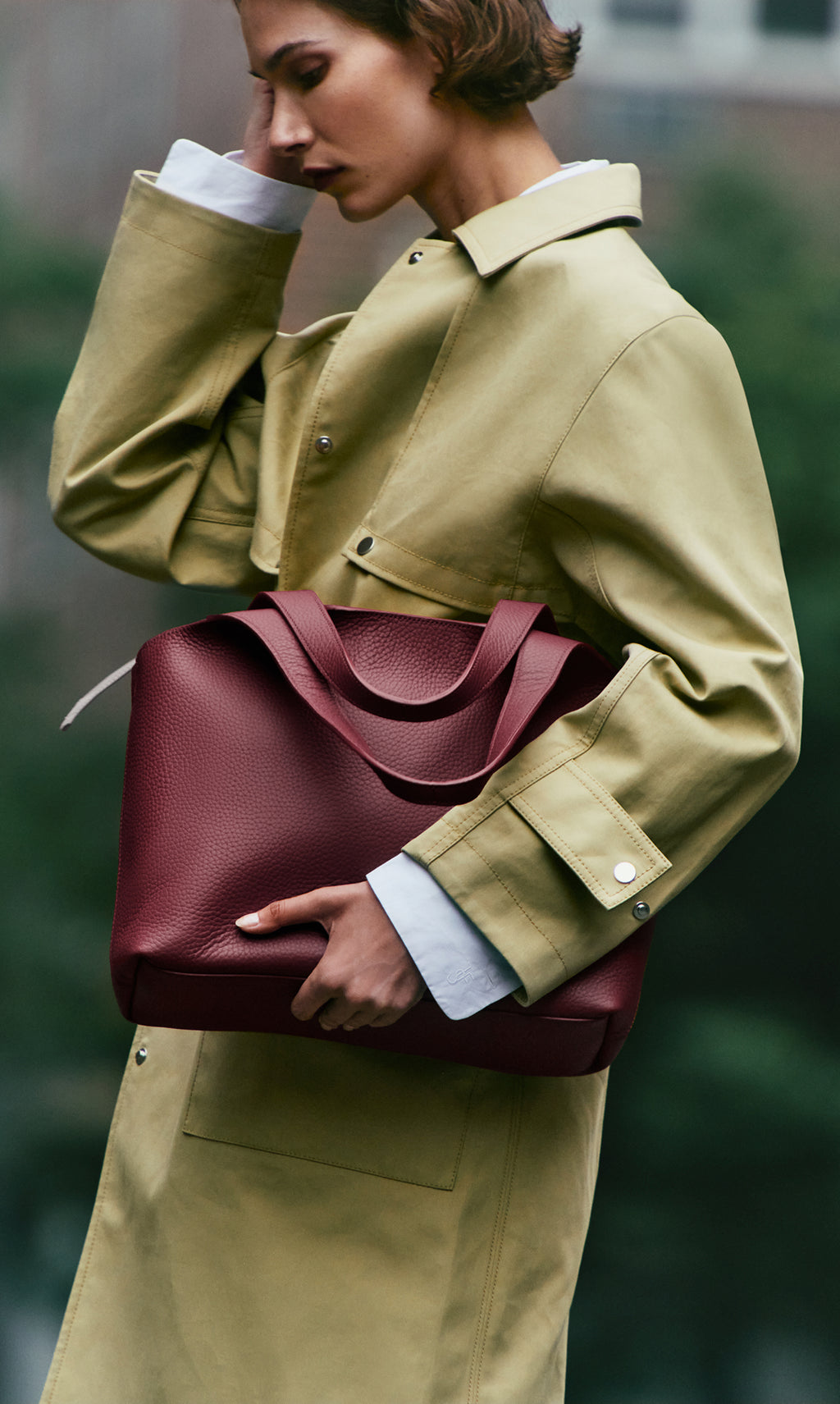 Person holding large handbag wearing a long coat outdoors.