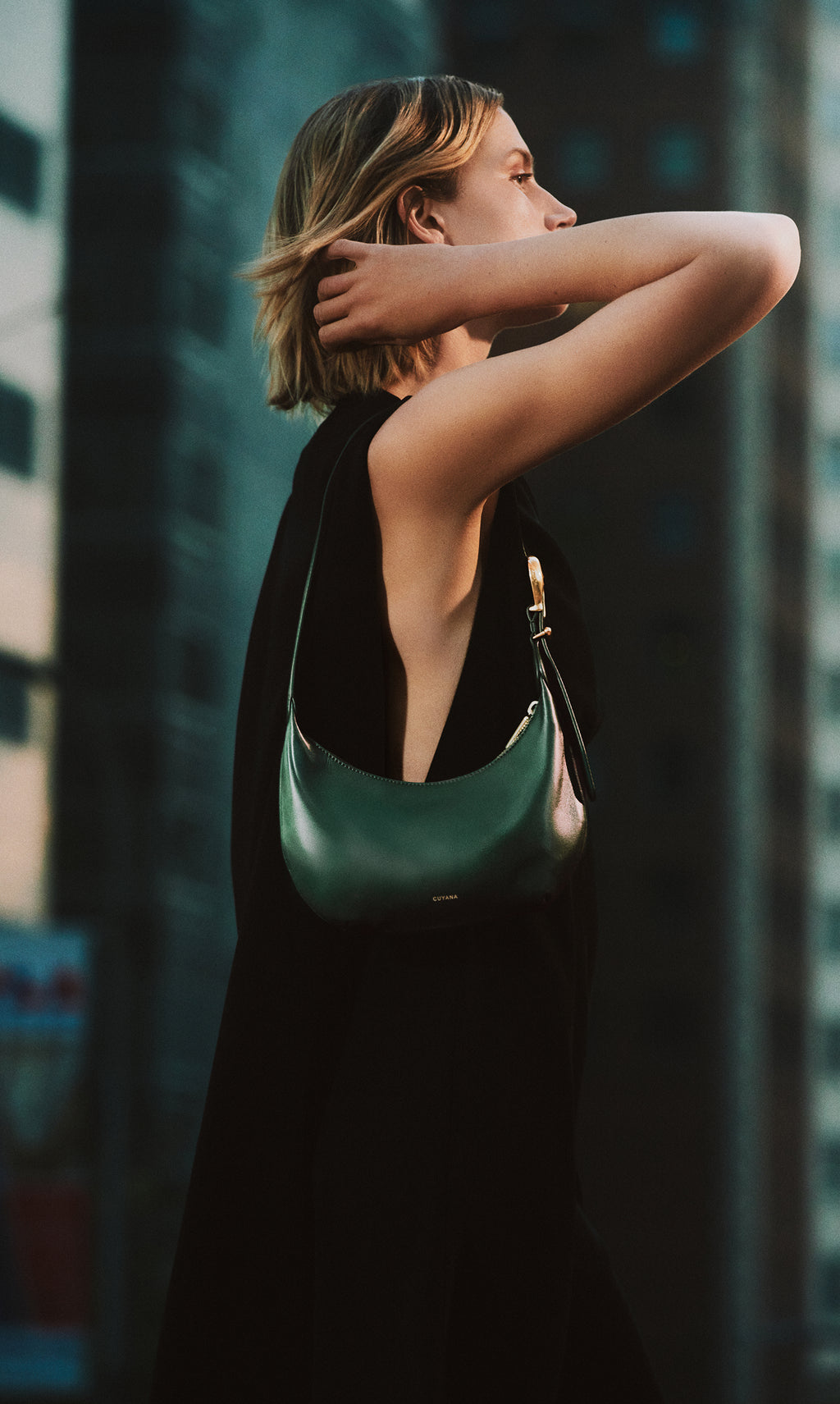 Person with shoulder bag stands near tall buildings.