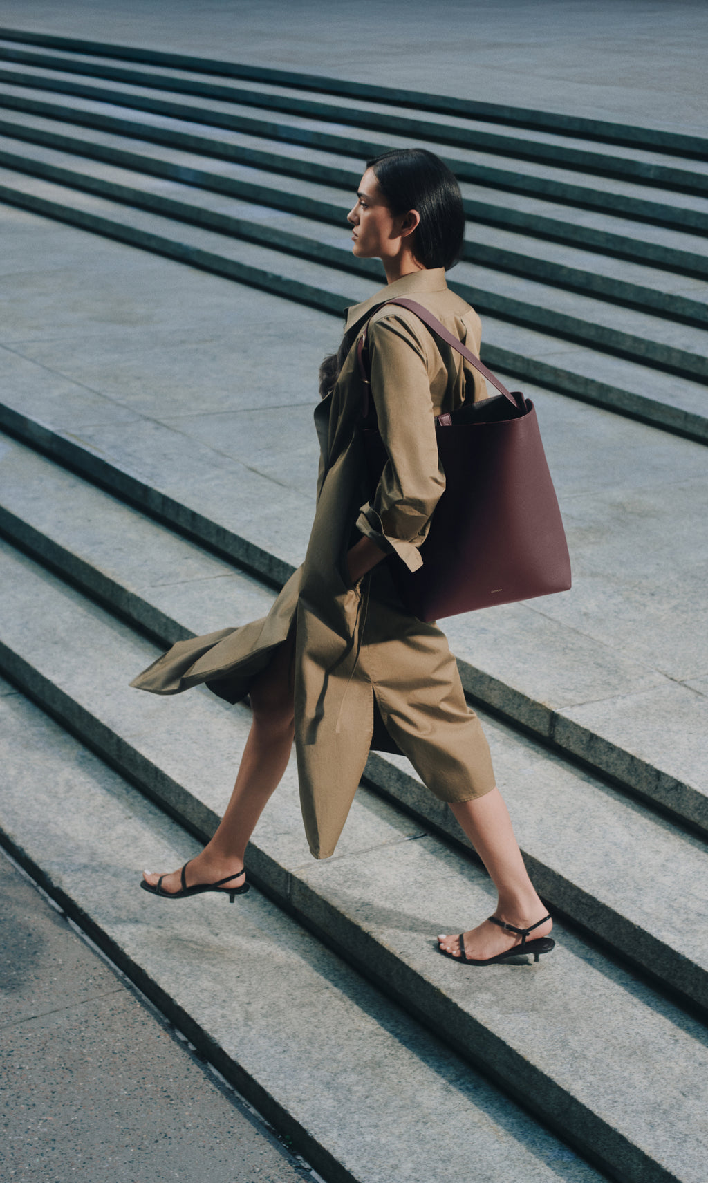 Person in a long coat walking up steps carrying a large bag