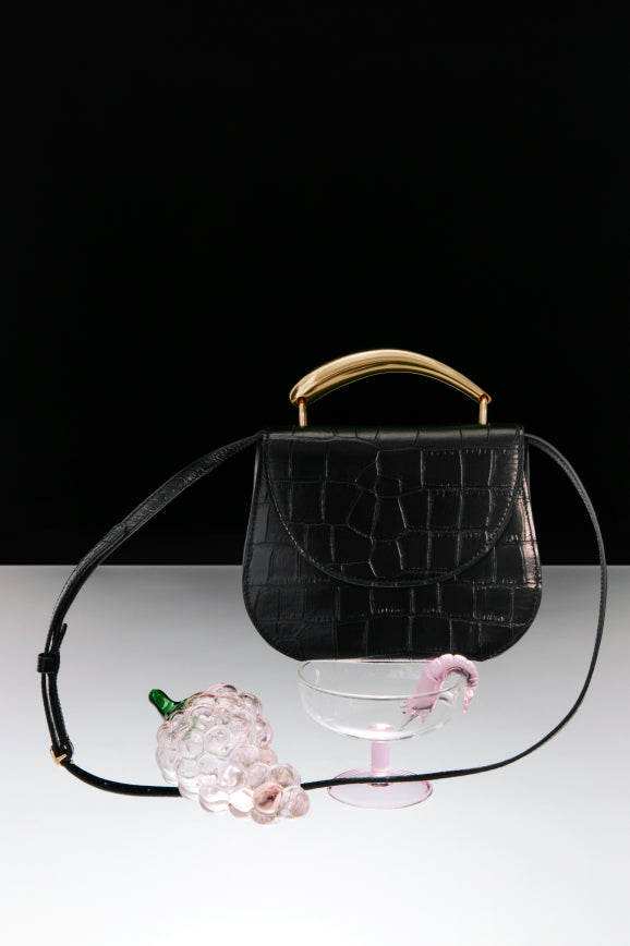 Handbag with a strap next to a glass bowl and a decorative object.