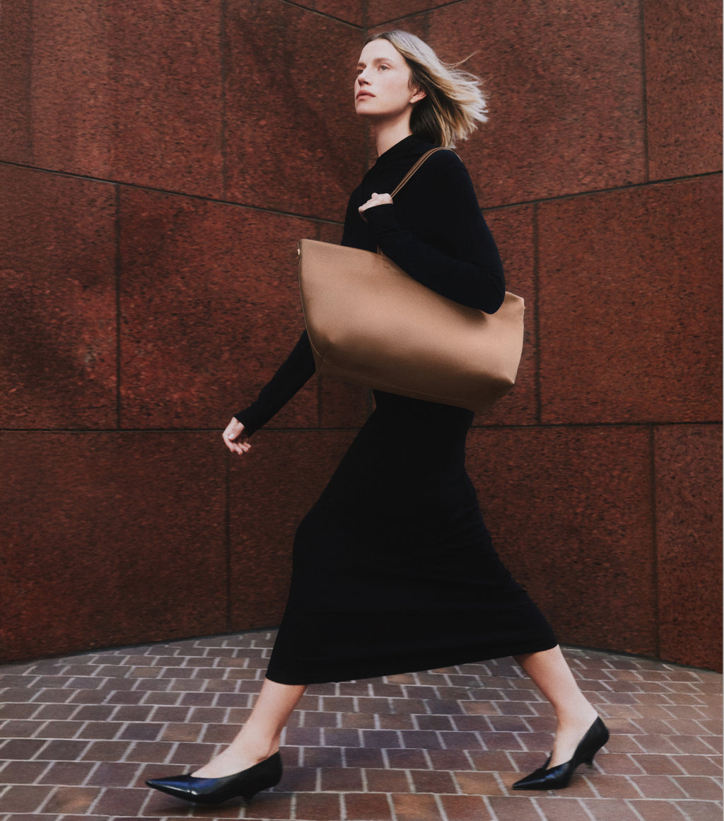 Person walking with large tote bag wearing long dress and pointed shoes.
